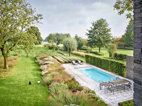 Blick ber den Garten am Stadtrand von Krefeld in die Tiefe der Landschaft: Pool, Terrasse, Staudenrabatten, Obstwiese