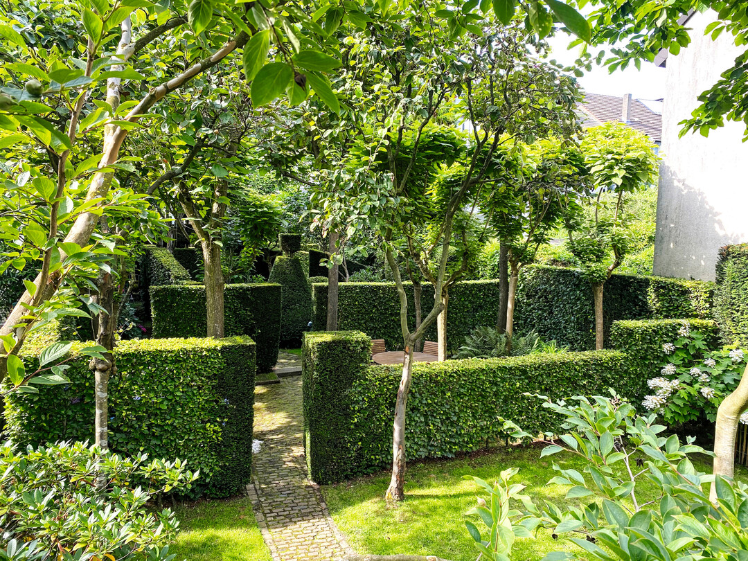Blick in das Catalpa-Gartenzimmer: ein Sitzplatz unter dem lichten Schatten der hohen Bäume