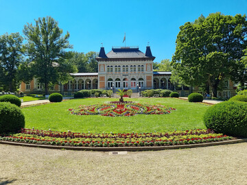 Das Königliche Kurhaus ist der Mittelpunkt von Bad Elster. Die Rasenfläche ist gerahmt von Wechselflor  mit einem zentralen Teppichbeet, in dessen Mitte eine Kanarische Dattelpalme (Phoenix canariensis) thront, wie zu Paul Schindels Zeiten.