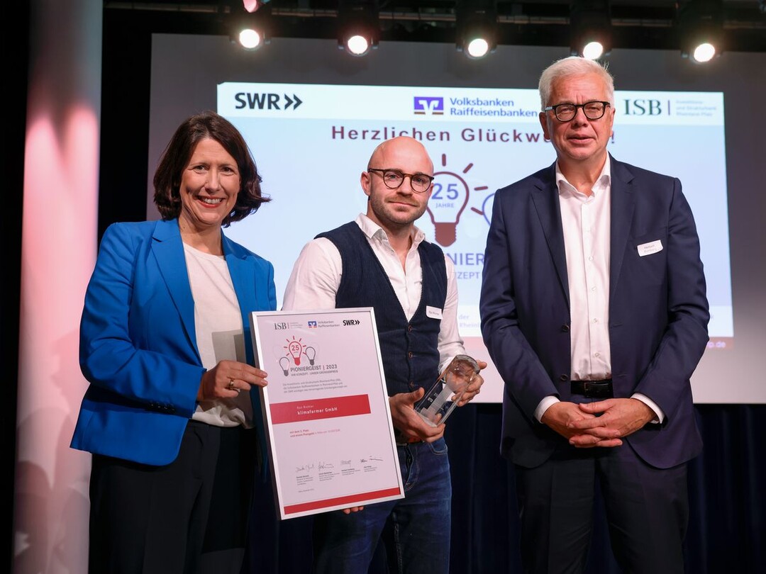 Ron Richter von der klimafarmer GmbH (mi.) erhält den Preis Pioniergeist 2023 von der rheinland-pfälzischen Wirtschaftsministerin Daniela Schmitt (li.) und Herbert Kohlberg von der Volksbank Darmstadt Mainz überreicht.